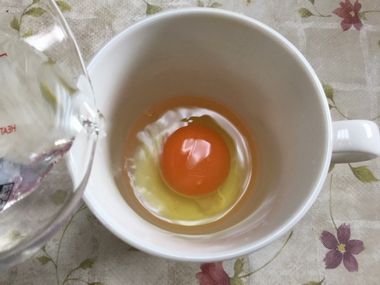 卵を割り入れたマグカップに水を注いでいます・